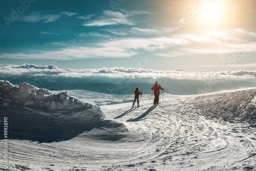 两个滑雪者在阳光灿烂的日子里登上山顶。