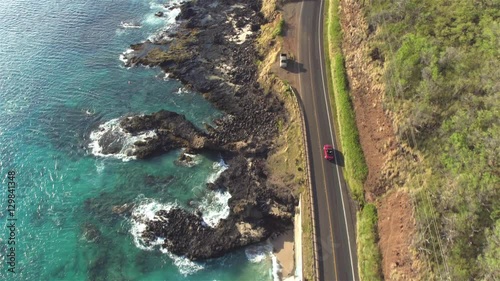 空中航拍:红色敞篷车行驶在令人惊叹的海岸公路上，上方是岩石海洋悬崖