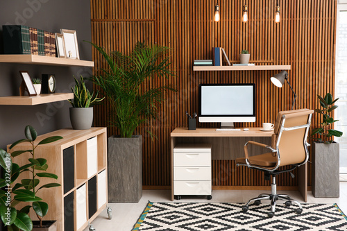舒适的工作场所，靠近木墙的电脑在时尚的房间内部。家庭办公室设计