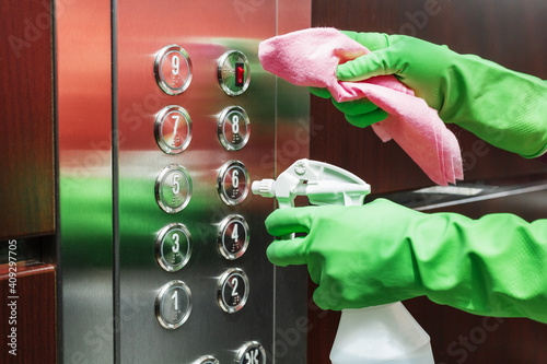 一位女士用消毒剂喷雾和湿纸巾清洁电梯按钮控制面板。